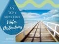 Long wooden walkway with white railing leading out to blue ocean.