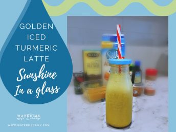 Turmeric latte in milk jug glass with straw on counter in front of ingredients.