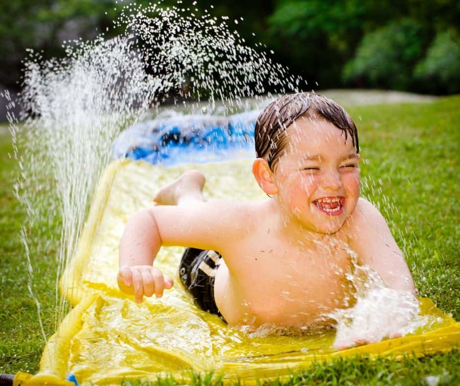 Smiling boy sliding down a wet slip and slide.